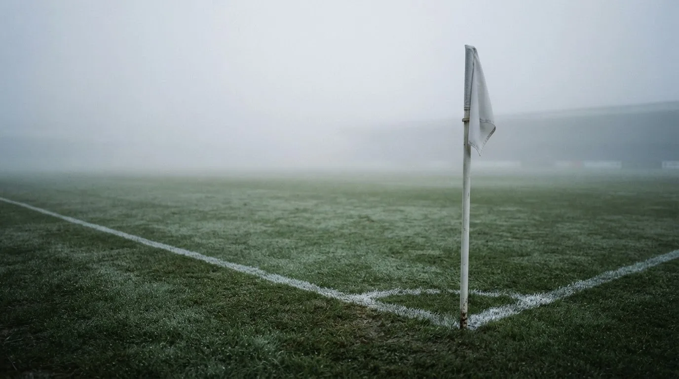 Der Rand eines Spielfelds mit weißer Linie und Eckfahne bei Nebel am frühen Morgen, ohne Menschen.