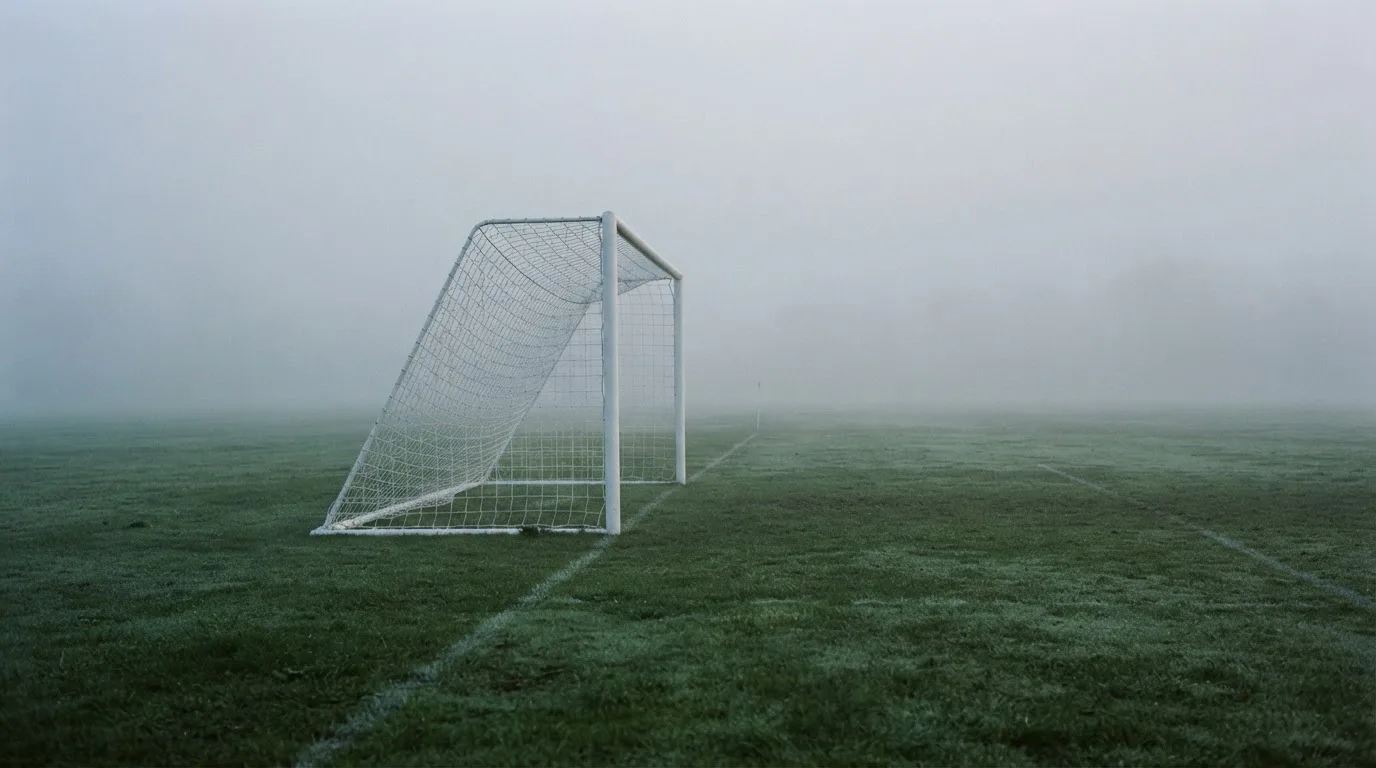 Ein Fußballtor mit Netz im Morgennebel auf einem leeren Platz, die Linien nur schwach zu erkennen.