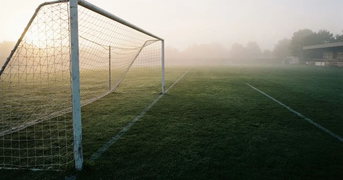Ein Fußballtor mit Netz steht auf einem leeren Platz im Nebel der Morgendämmerung, der Rasen ist taufeucht.