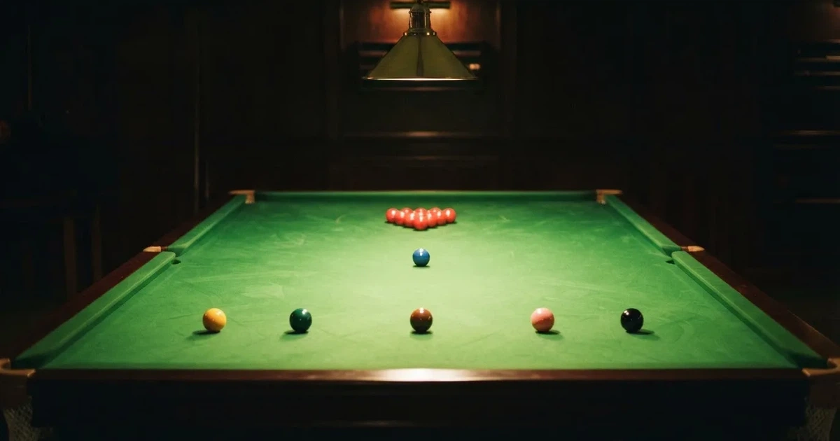 Ein Snookertisch mit grünem Tuch und aufgebauten roten Kugeln in einem abgedunkelten Raum unter einer hängenden Lampe.