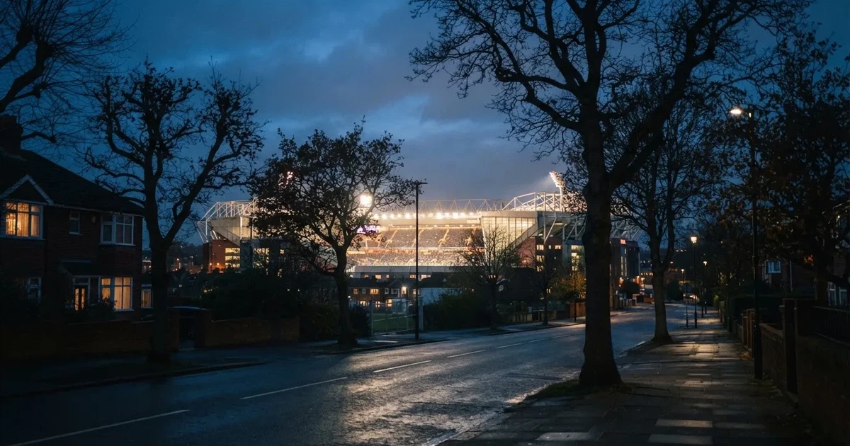 Ein hell erleuchtetes Stadion aus der Ferne bei Nacht, davor eine stille Straße und ein paar Bäume.