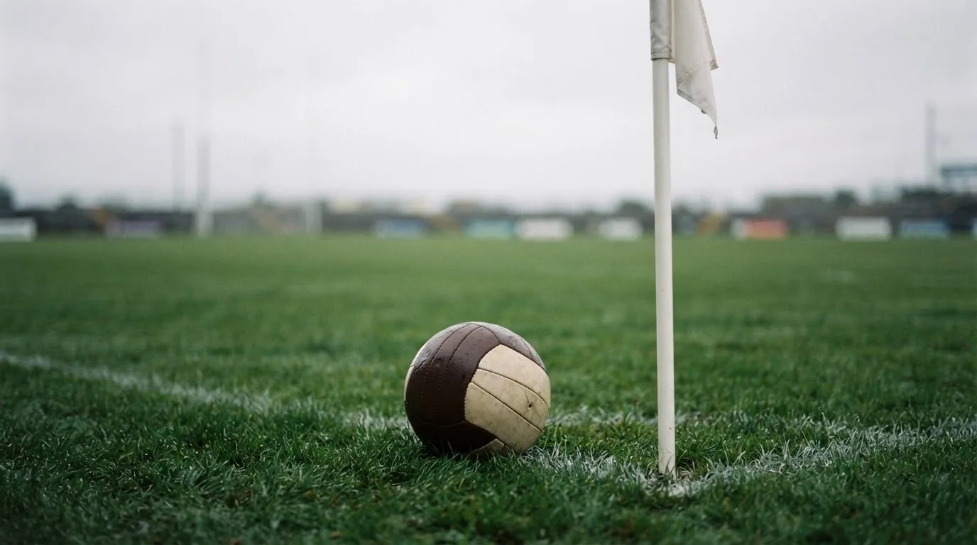 Ein Fußball liegt neben einer Eckfahne auf kurz gemähtem Rasen unter bewölktem Himmel.